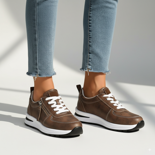 Brown sneakers with white laces worn with light blue jeans on a neutral background