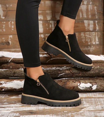 Black ankle boots with zippers worn by a person on wooden logs.