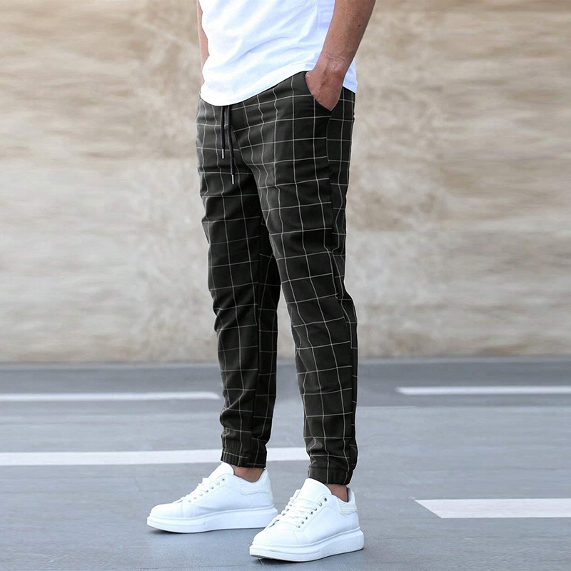 Person wearing black checkered pants and white sneakers on a plain background