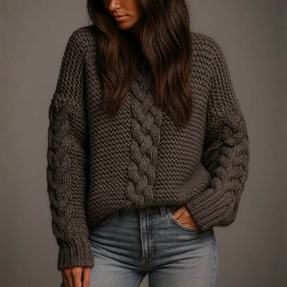 Person wearing a chunky knit sweater and jeans against a plain background