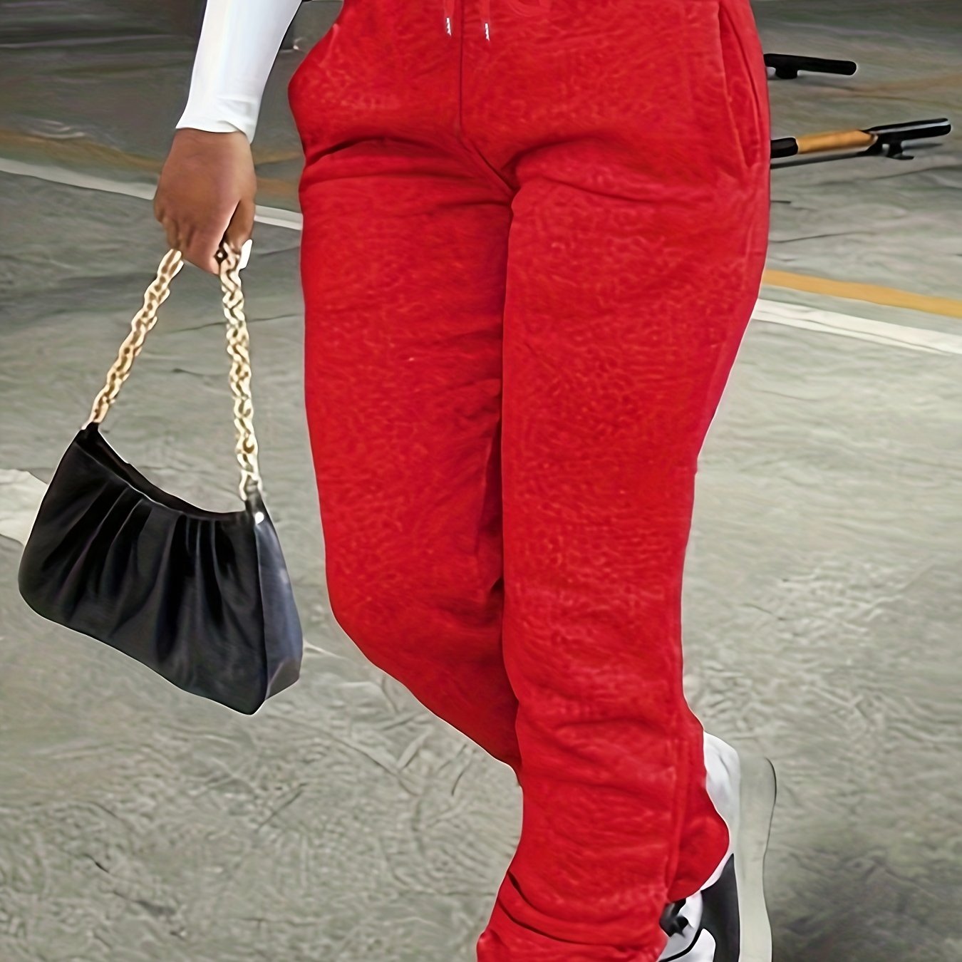 Person wearing red pants holding a black handbag with gold chain strap.
