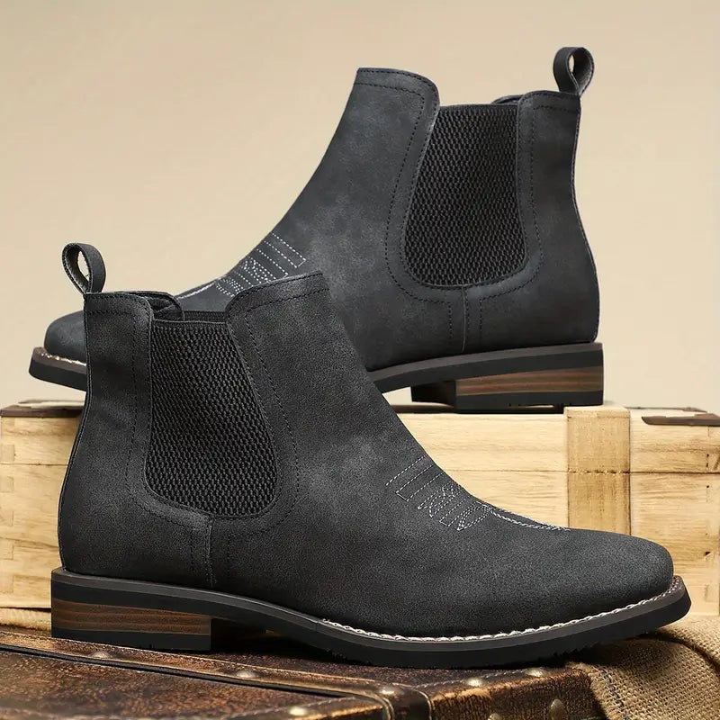 Pair of black suede Chelsea boots on a wooden surface with a beige background