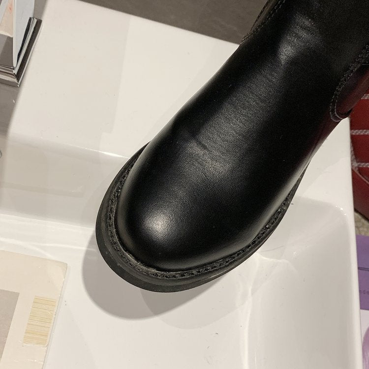 Black leather boot on a white surface with a blurred background