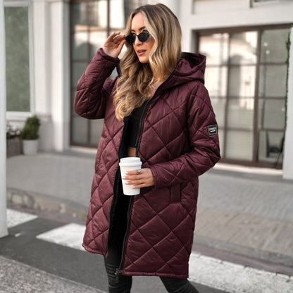 Woman wearing a maroon quilted coat holding a white cup outdoors.