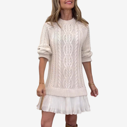 Woman wearing a cream cable knit sweater over a white skirt on a white background