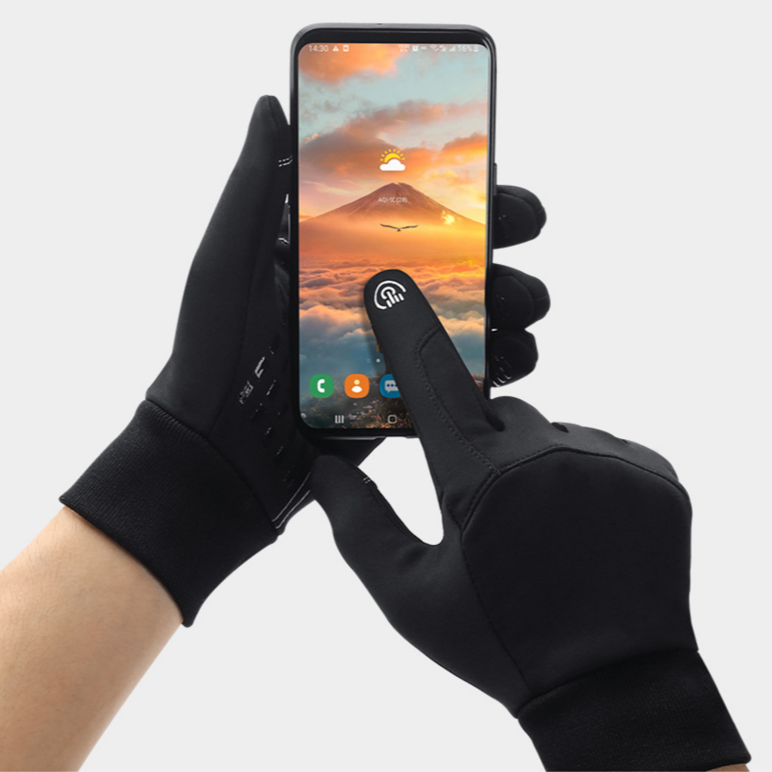 Person wearing black gloves holding a smartphone with a mountain and sunset display.