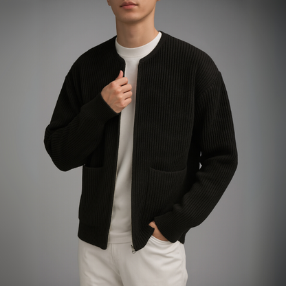 Person wearing a black ribbed sweater over a white shirt and pants on a gray background
