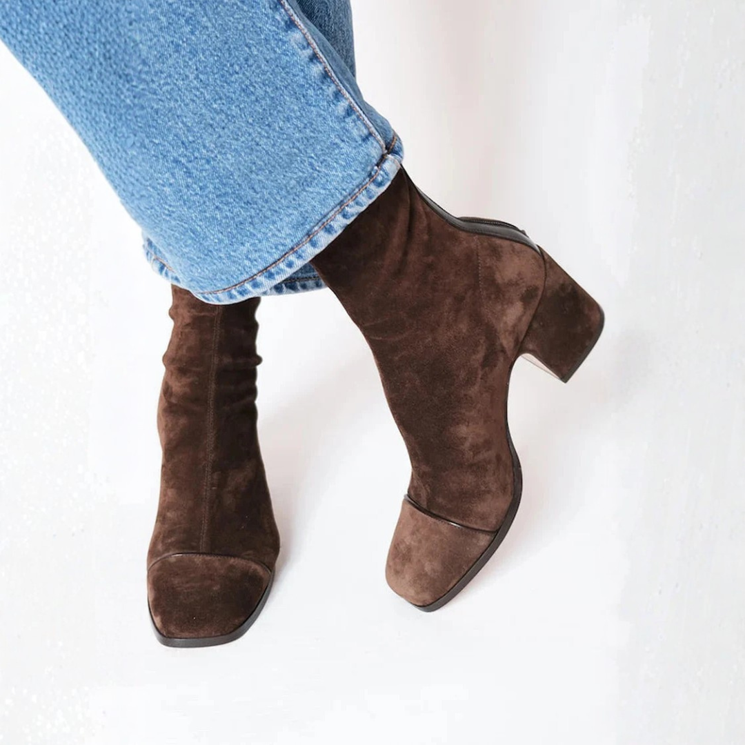 Brown suede boots worn with blue jeans on a white background