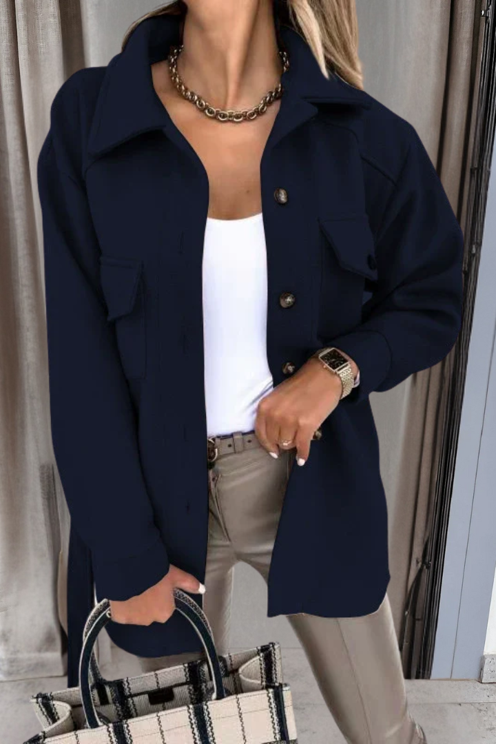 Person wearing a navy blue coat with a white top and beige pants, holding a black and white bag.