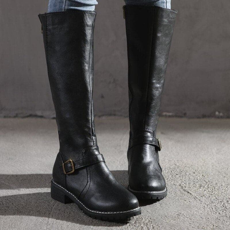 Black knee-high boots with buckles on a gray surface