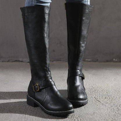 Black knee-high boots with buckles on a gray surface