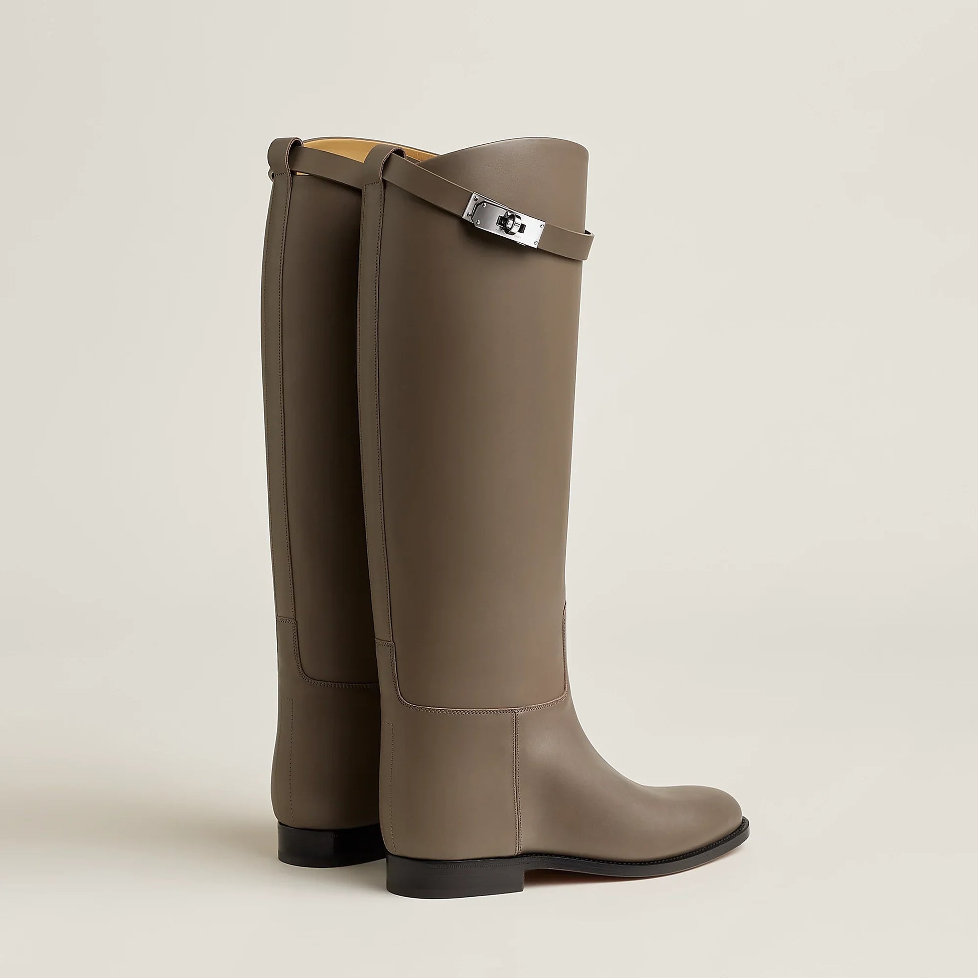 Pair of brown knee-high boots with a strap on a beige background
