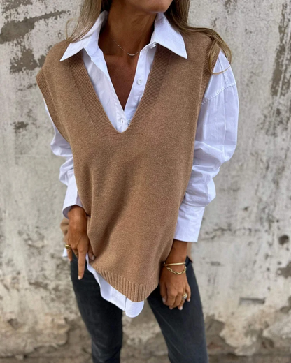 Person wearing a brown sweater vest over a white shirt against a textured wall.