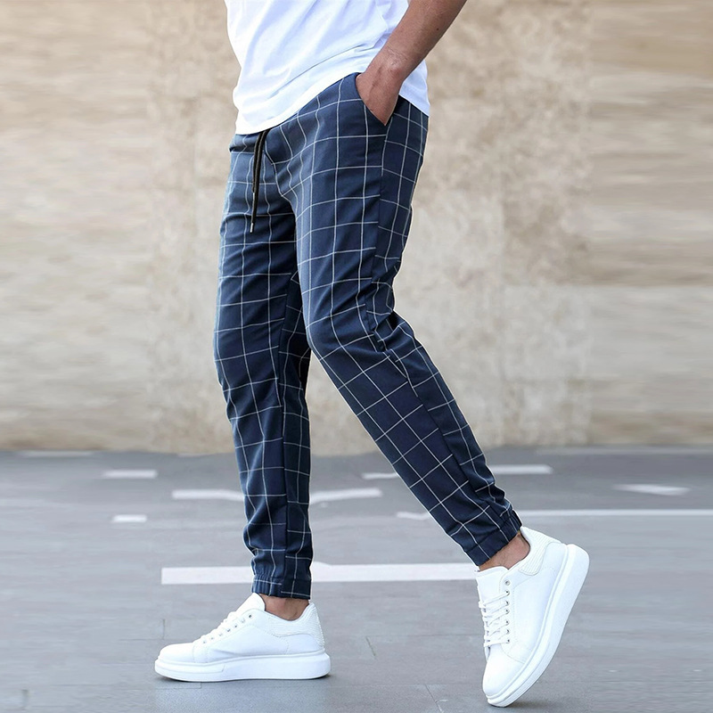 Person wearing navy checkered pants and white sneakers on a plain background