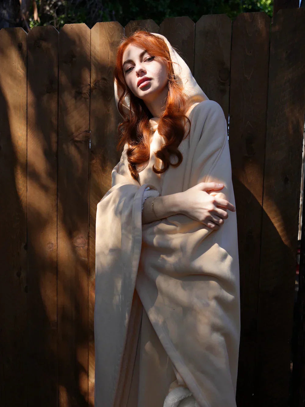 Woman in a white dress with red hair standing against a wooden fence.