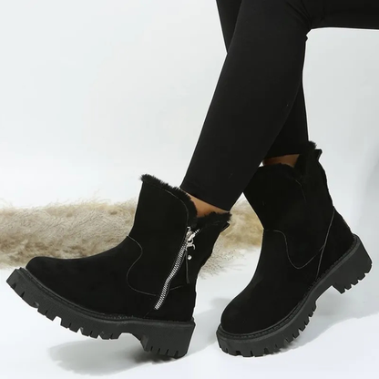 Black ankle boots with fur lining and zippers worn by a person on a white background