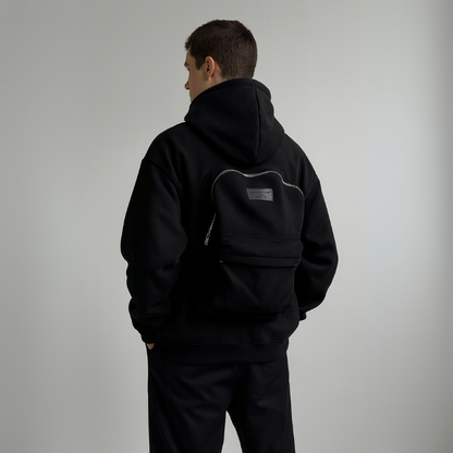 Person wearing a black hoodie with a small logo on the back against a plain background