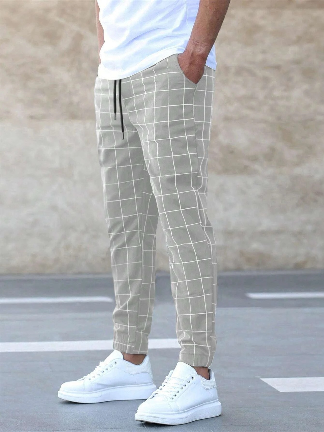 Person wearing light gray checkered pants and white sneakers on a neutral background