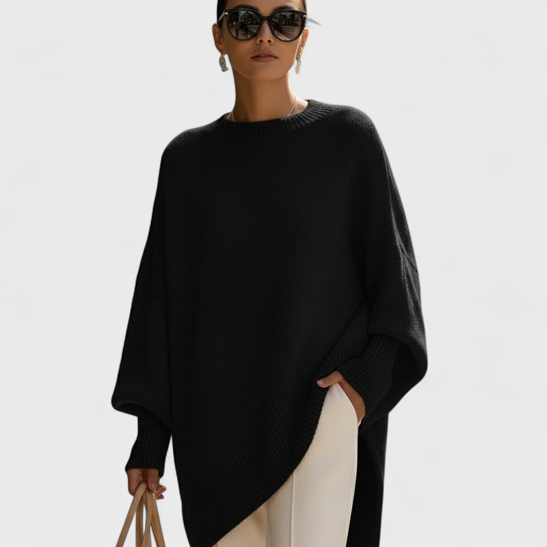 Woman wearing a black poncho and sunglasses on a light gray background