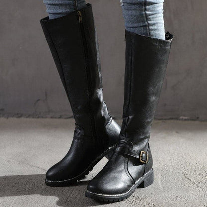 Black knee-high boots with buckles worn by a person on a gray background
