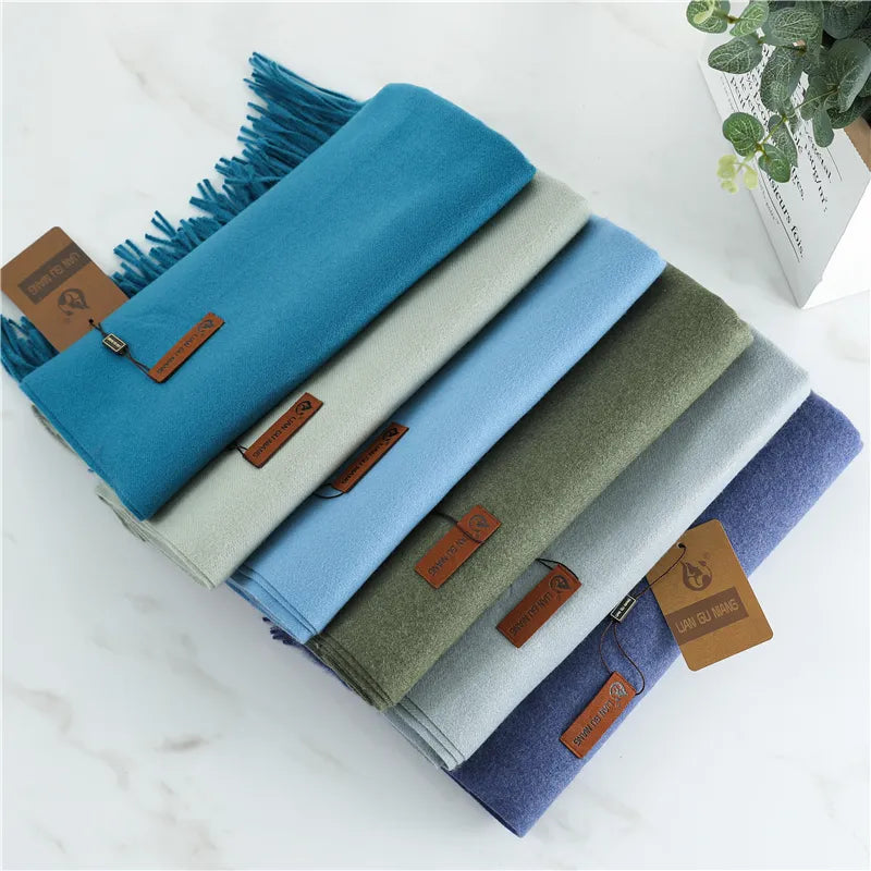 Stack of folded scarves in various colors with brown leather tags on a white surface.