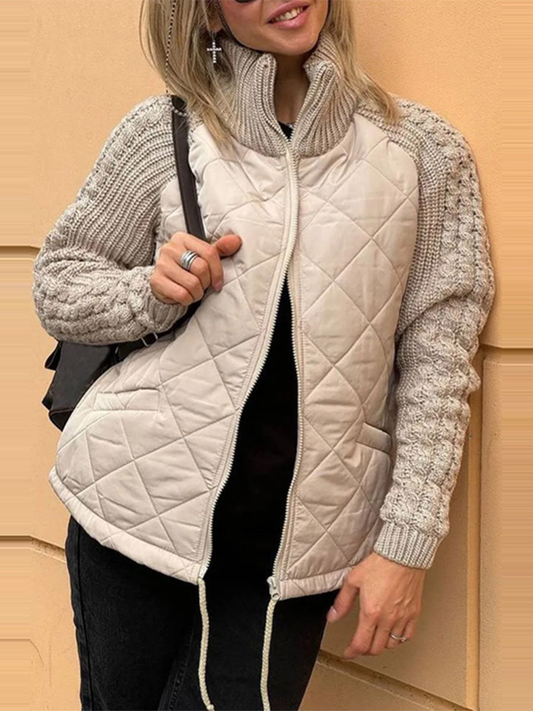 Person wearing a beige quilted vest over a knitted sweater against a beige wall.