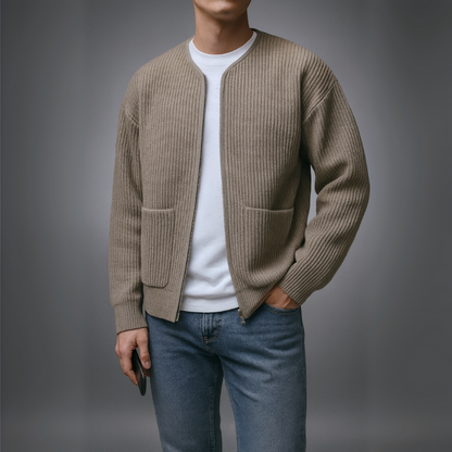 Person wearing a beige cardigan over a white shirt and blue jeans on a gray background