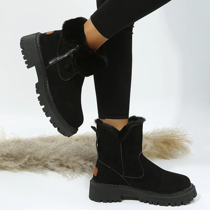 Black suede boots with fur trim worn by a person on a white background