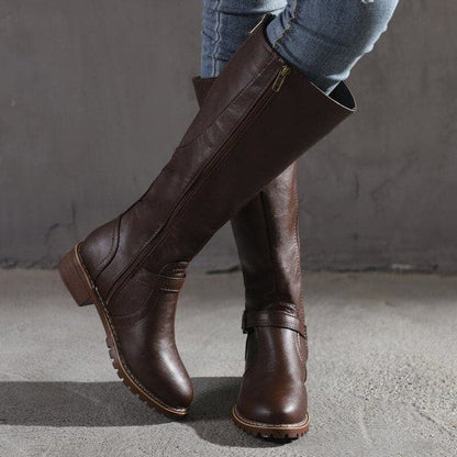 Brown knee-high boots worn with jeans against a gray background