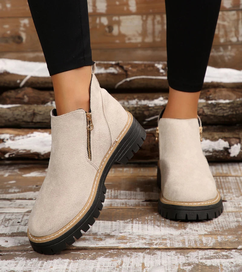 Beige ankle boots with black soles on a wooden floor.