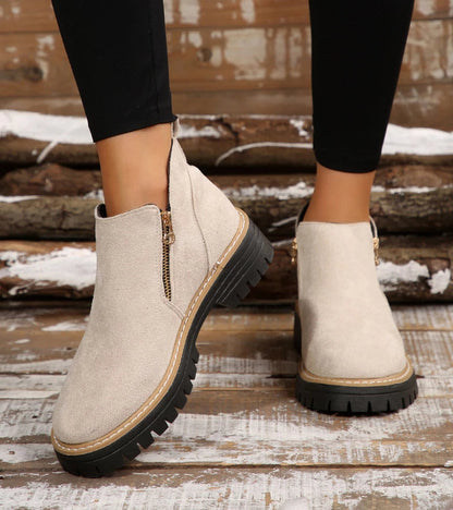 Beige ankle boots with black soles on a wooden floor.