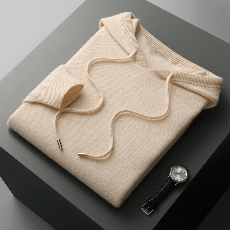 Folded beige hoodie on a dark surface with a watch