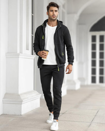Man in black tracksuit with white shirt holding a coffee cup, standing in a classical architectural setting.