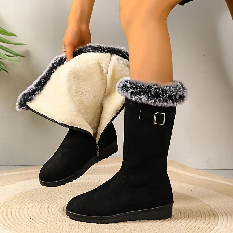 Black winter boots with fur trim worn by a person on a neutral background