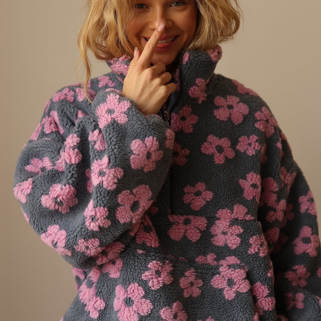 Person wearing a dark gray fleece jacket with pink floral patterns, posing with a finger on their lips.