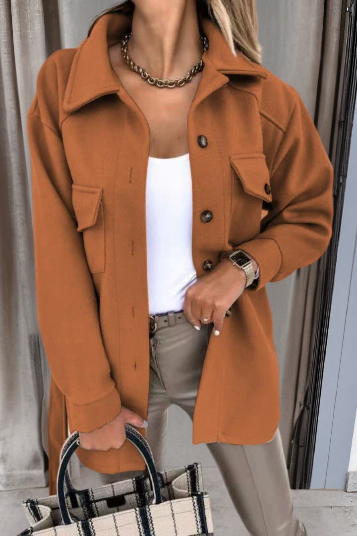 Person wearing a brown coat with a white top and beige pants, holding a black and white bag.