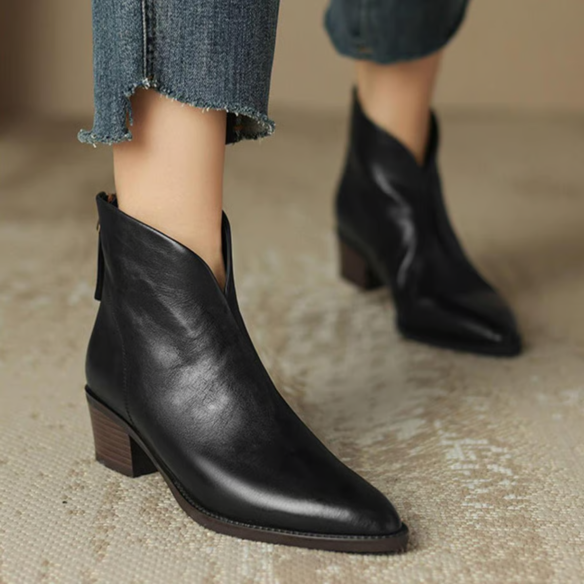 Black ankle boots worn with jeans on a neutral background