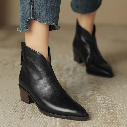 Black ankle boots worn with jeans on a neutral background