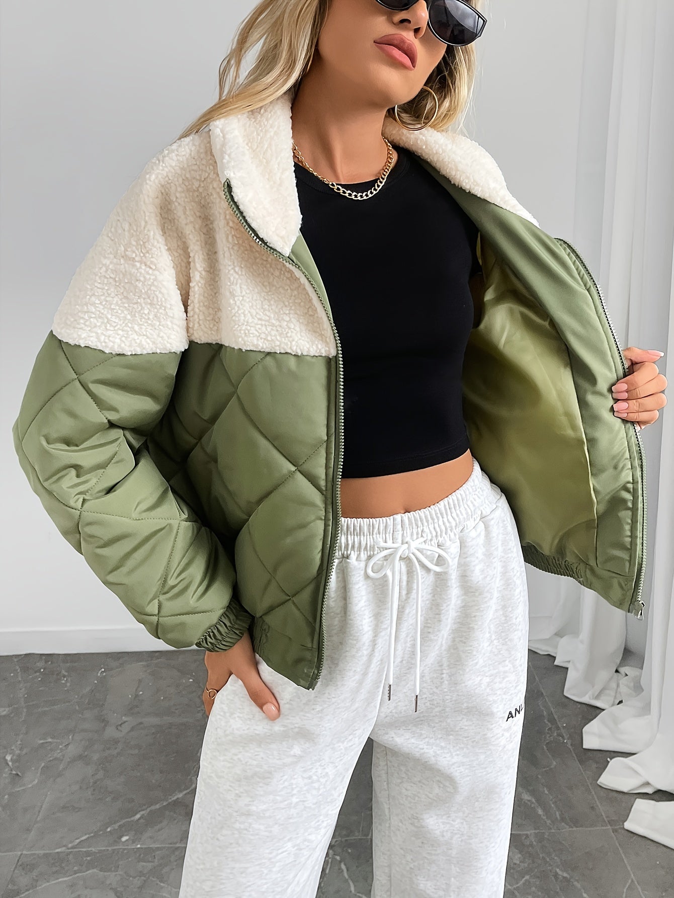 Woman wearing a green and white jacket with a black top and white pants on a gray floor.