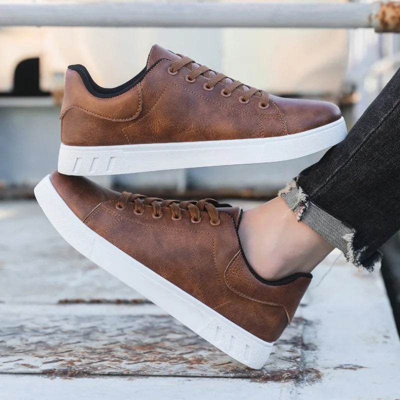 Brown leather sneakers with white soles worn by a person on a wooden surface.