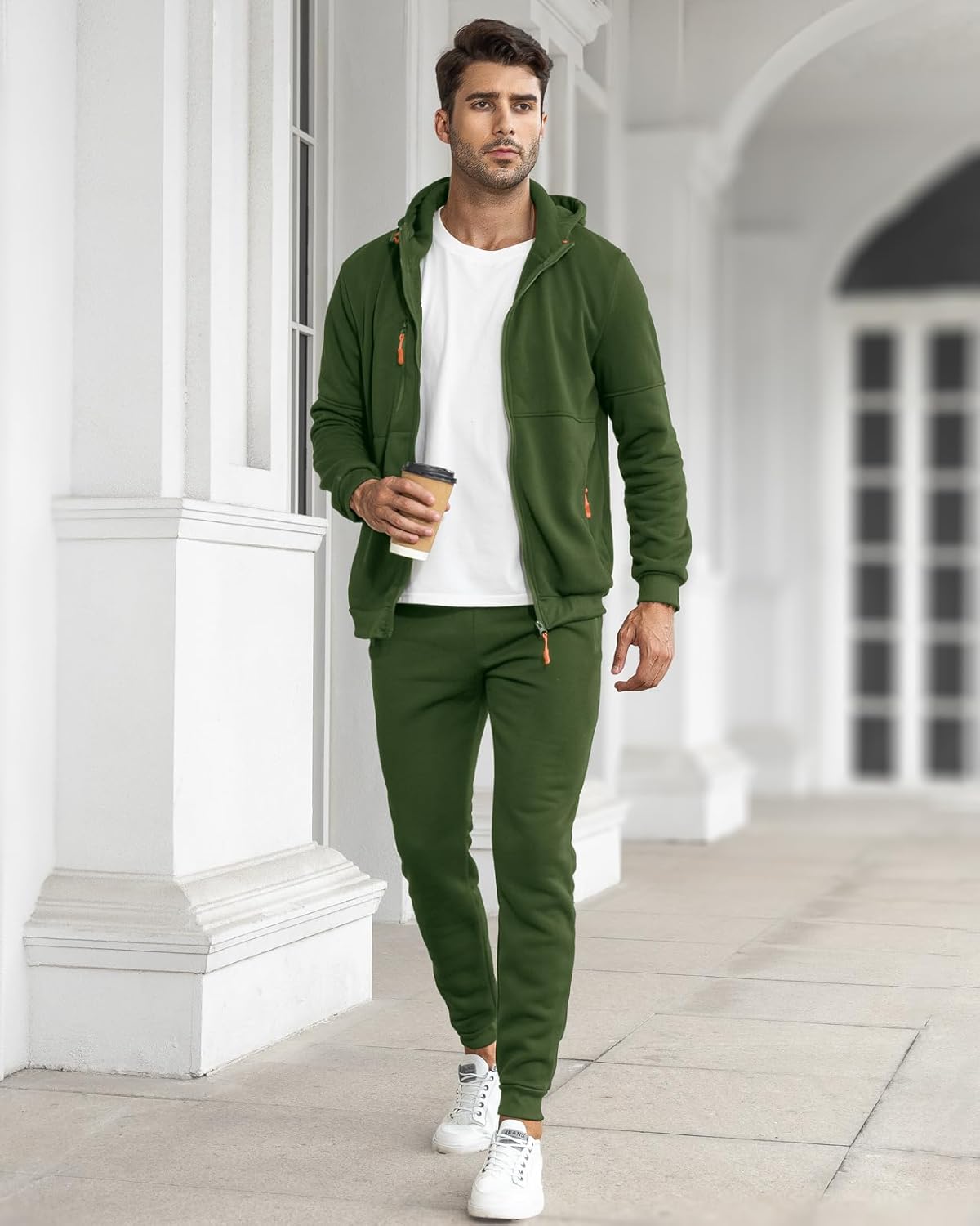Man wearing a green tracksuit holding a coffee cup in an elegant interior setting