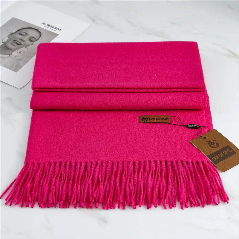 Hot pink scarf with fringes on a white surface, featuring a brand tag.