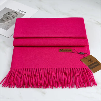 Hot pink scarf with fringes on a white surface, featuring a brand tag.