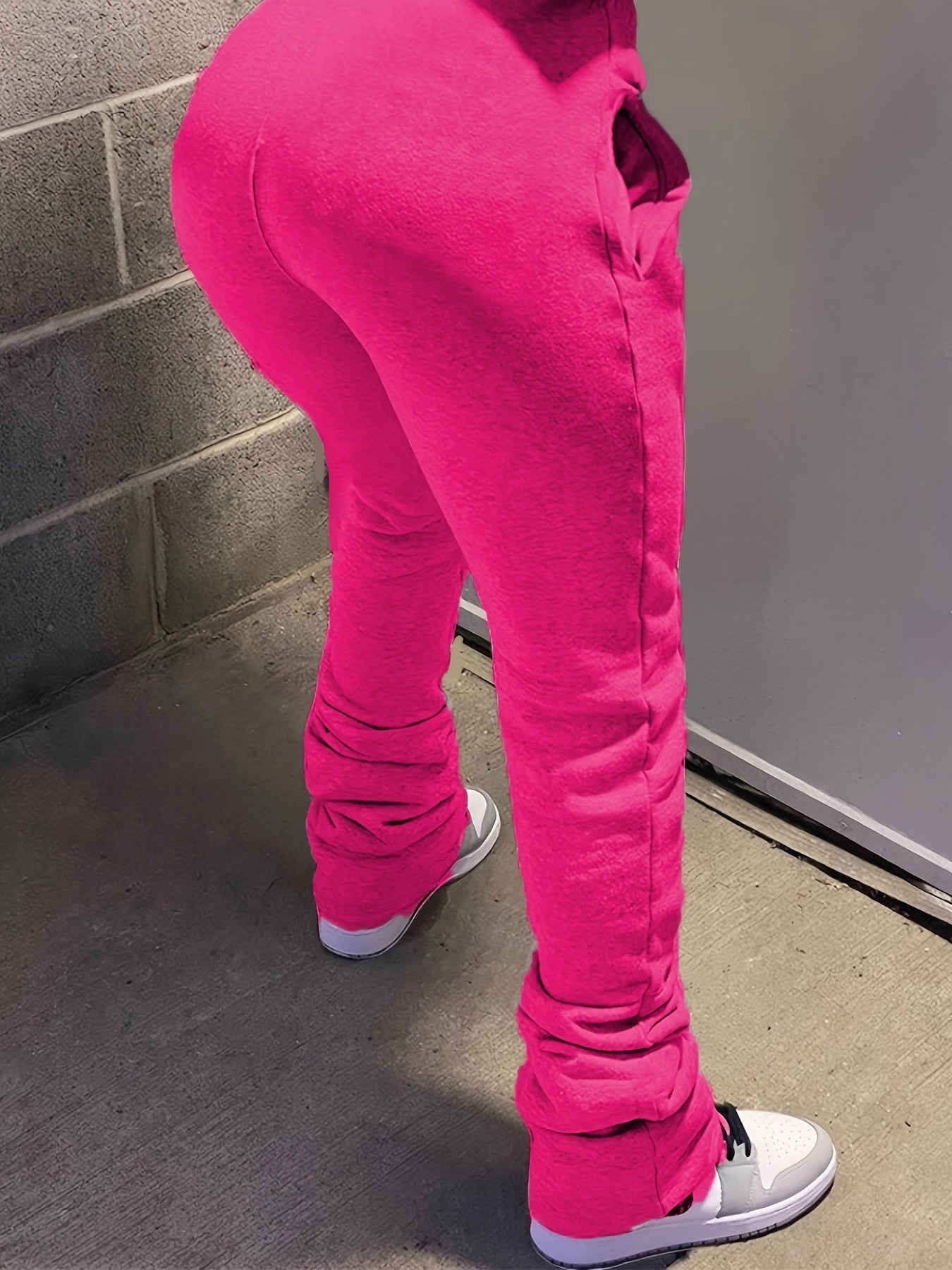 Person wearing bright pink pants and white shoes standing against a gray wall.
