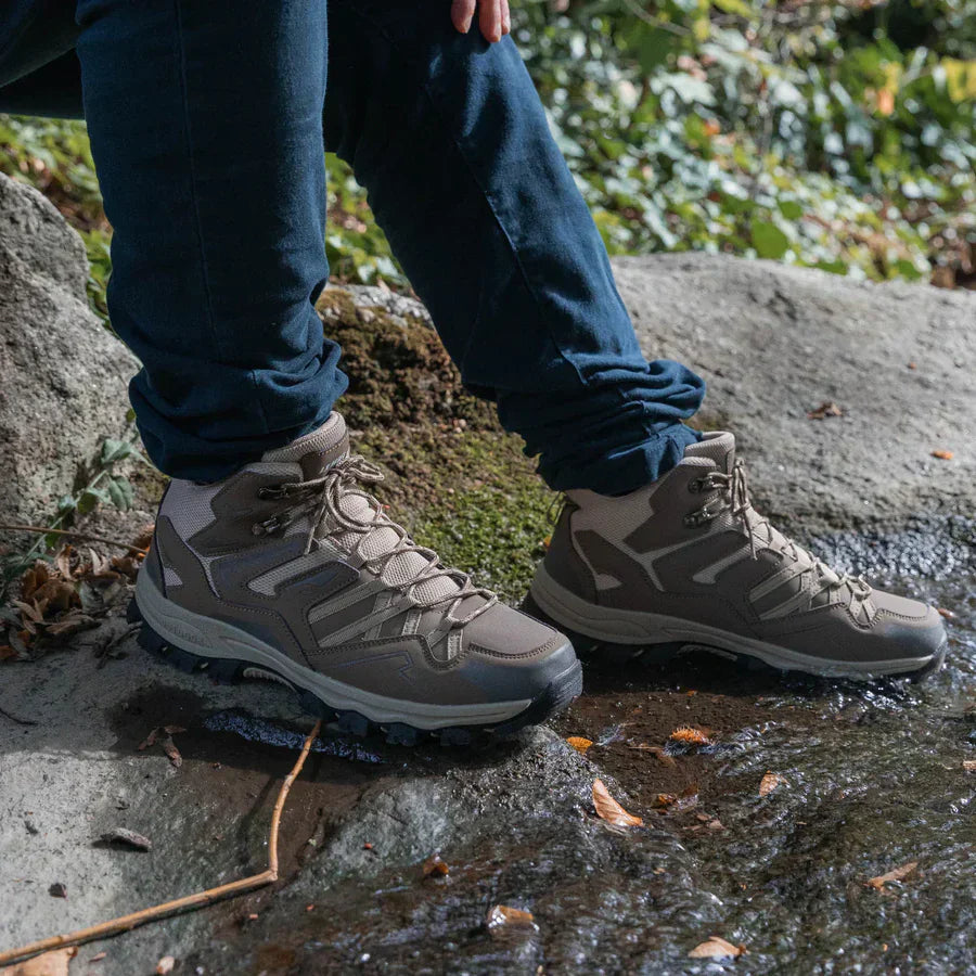 Person wearing hiking boots on a rocky surface with greenery in the background