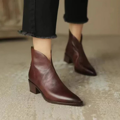 Brown leather ankle boots worn with black pants on a neutral background