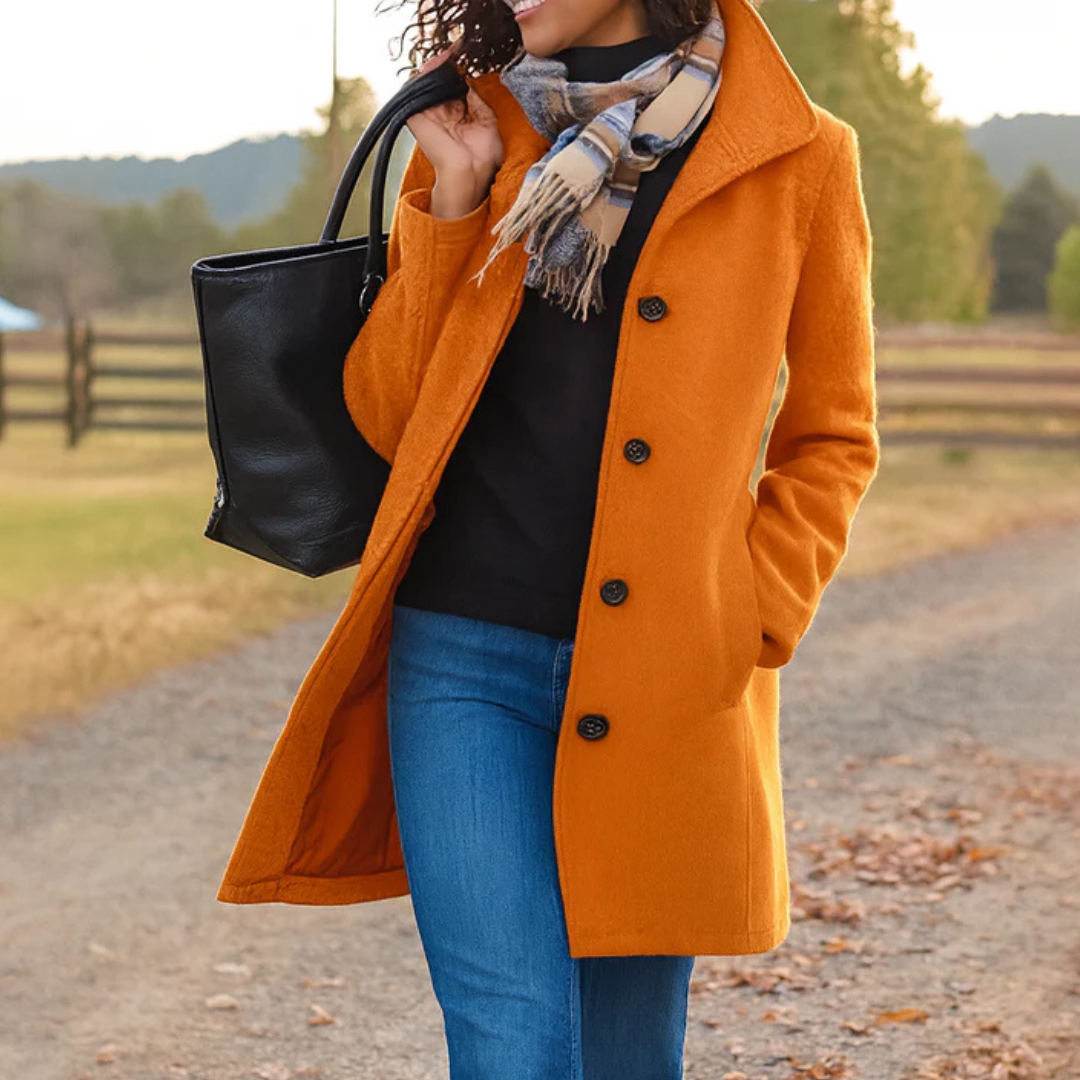 Person wearing an orange coat, black sweater, blue jeans, and plaid scarf outdoors.