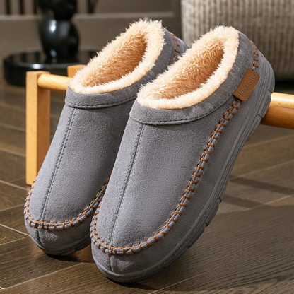 Pair of gray slippers with brown interior and stitching on a wooden floor.