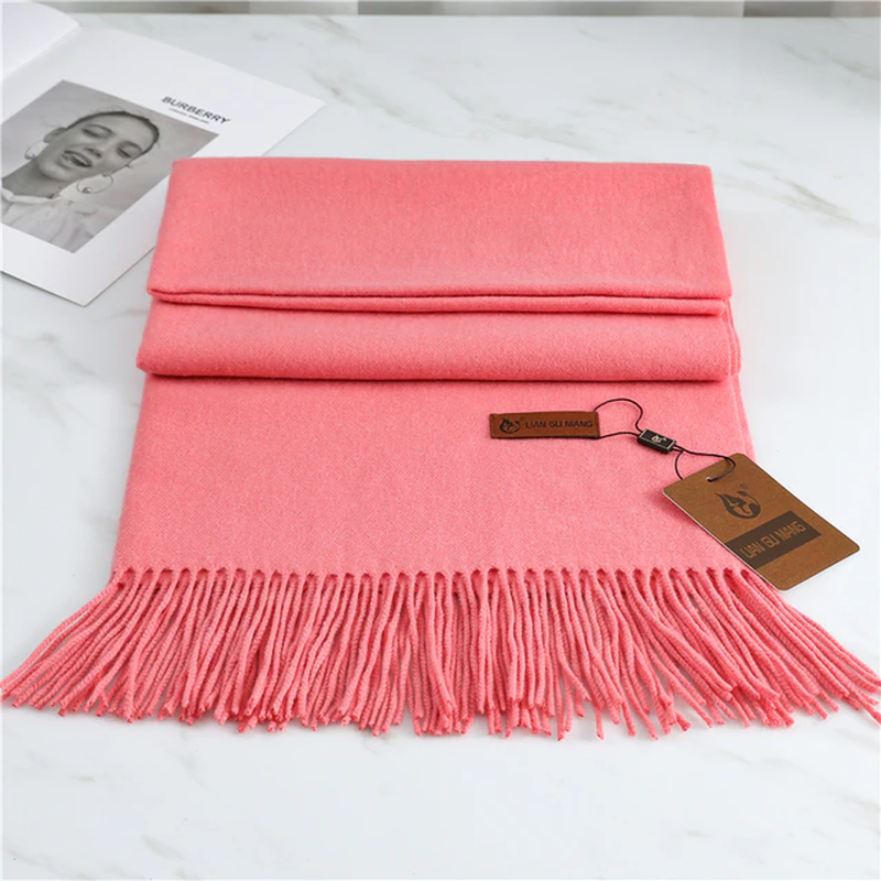 Pink scarf with fringe on a white surface, featuring a brand tag.