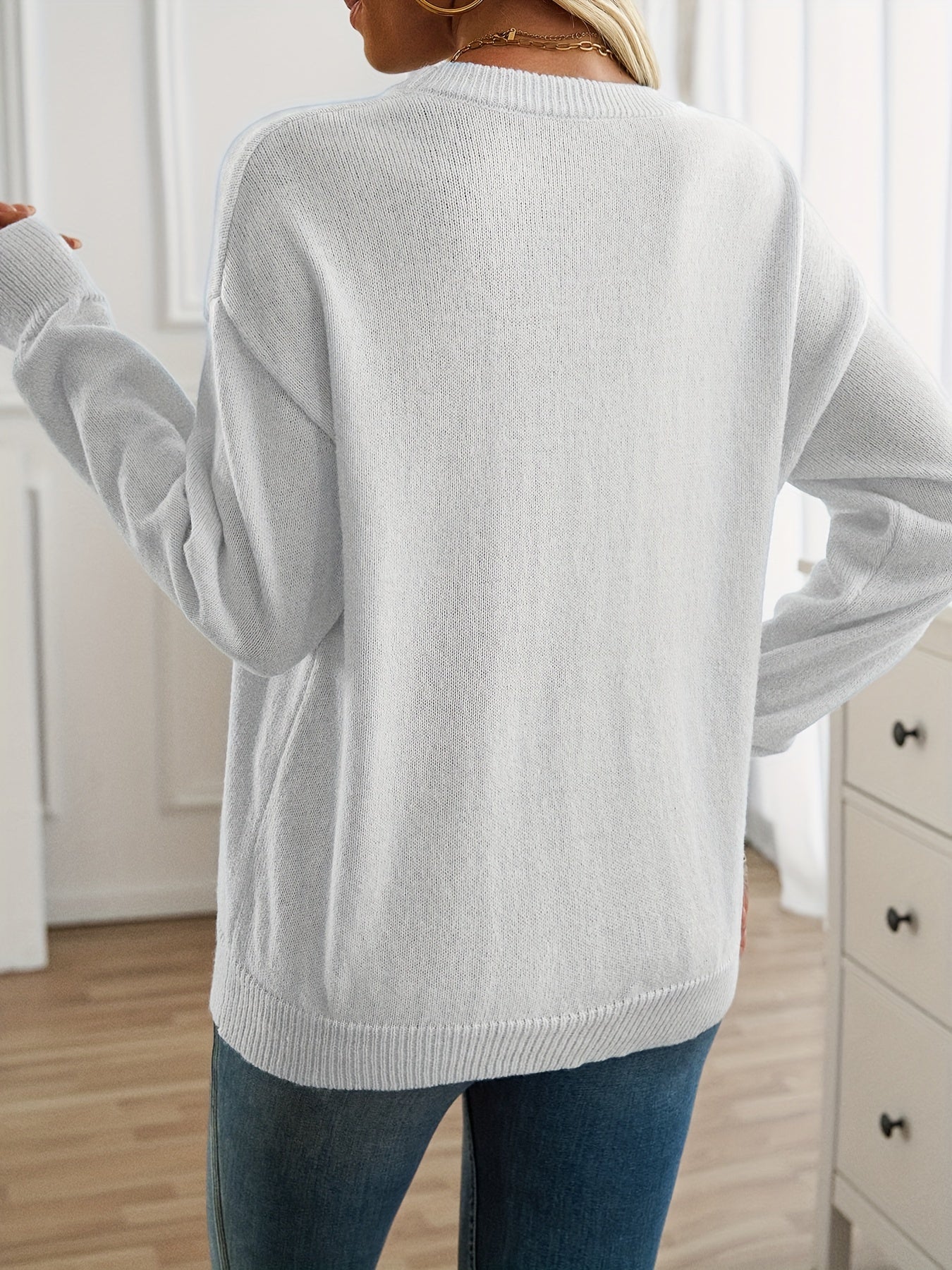 Person wearing a light gray sweater in a room with white walls and wooden flooring.